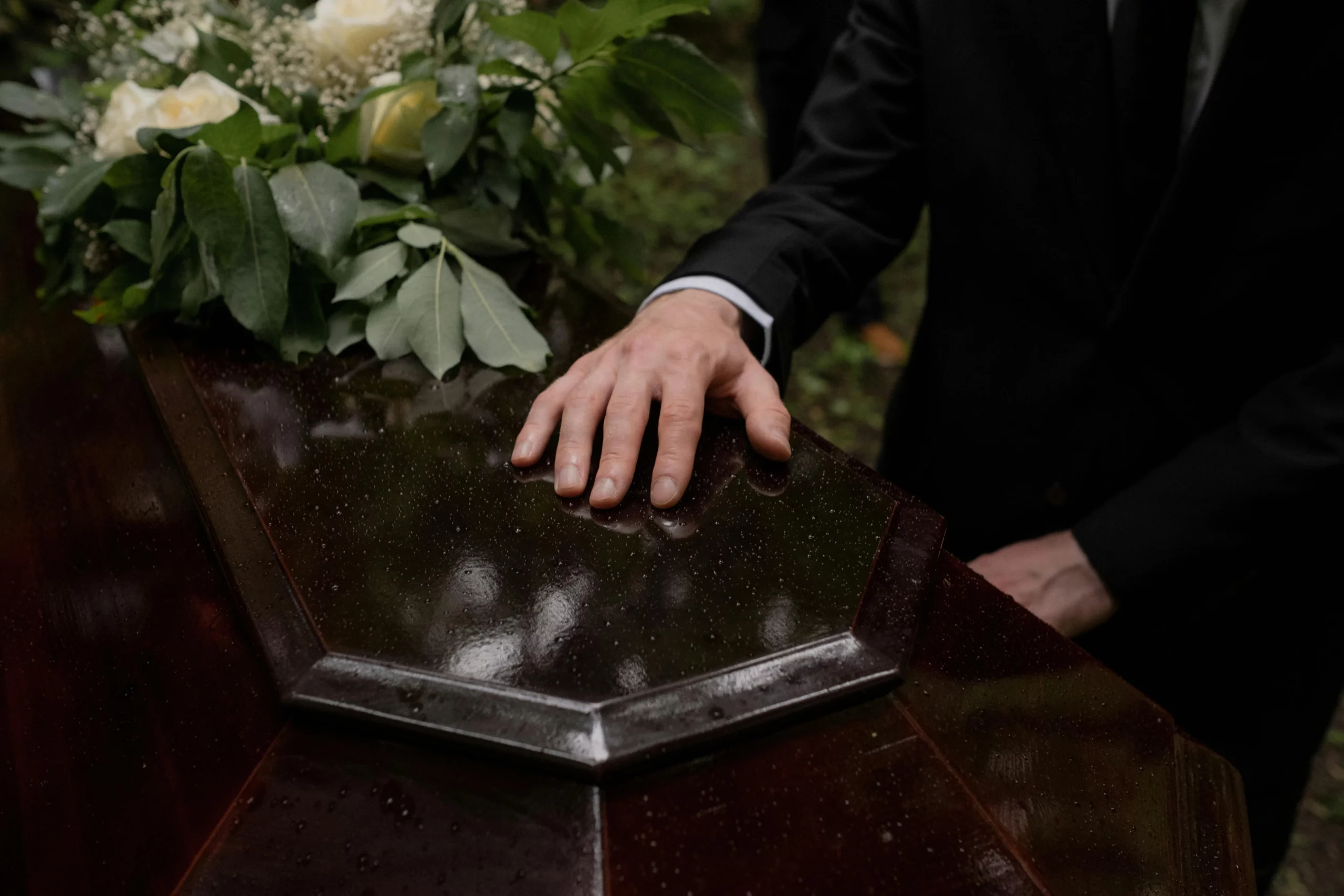 Main posée avec recueillement sur un cercueil sombre et verni pendant une cérémonie de deuil